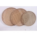 A series of graduated whicker trays of circular form being handwoven.  6cm x 70cm