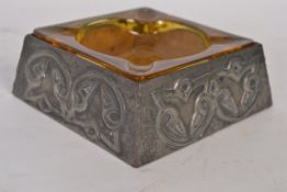 An Arts & Crafts pewter ashtray with inset glass amber liner in the manner of Archie Knox.