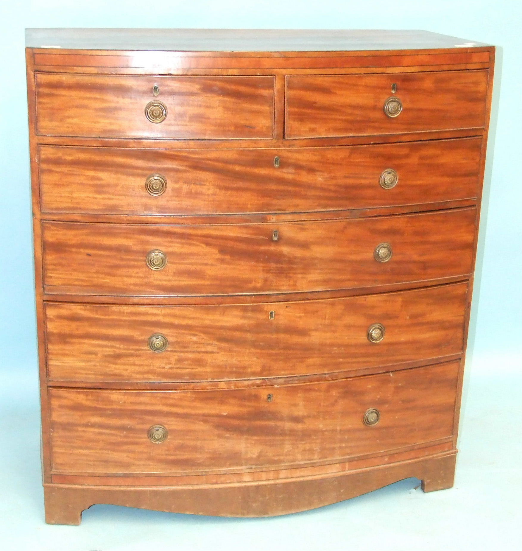 An early-19th century mahogany bow-front chest of two short and three long cock-beaded drawers, on