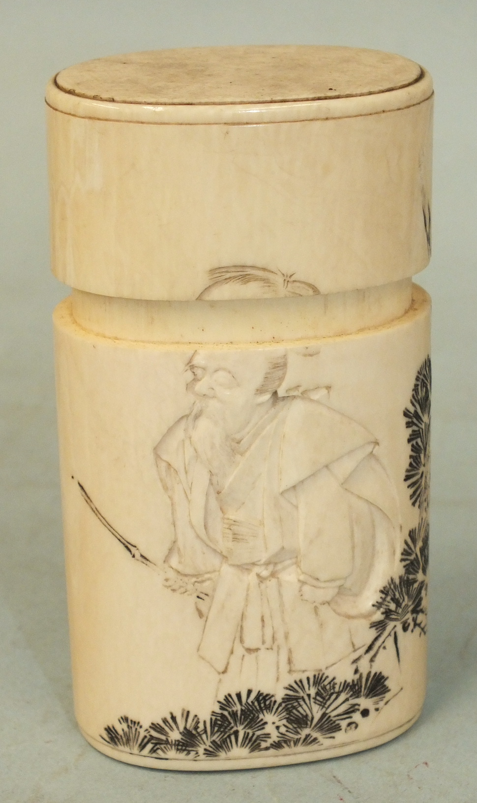 A Japanese ivory oval tall box and cover carved with an old man and bamboo branches, signed to