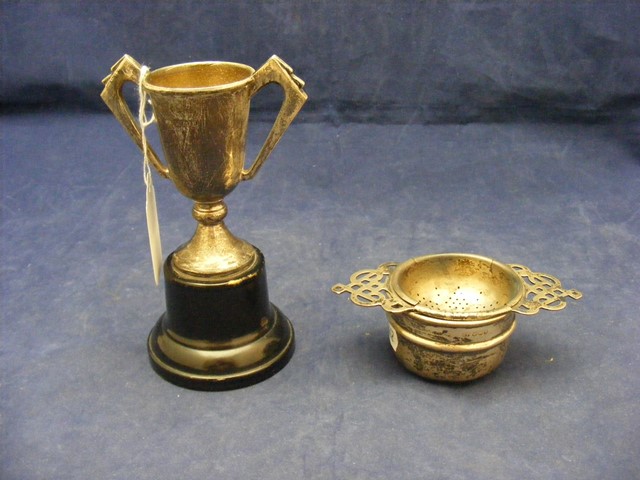 A silver tea strainer together with a silver trophy on stand