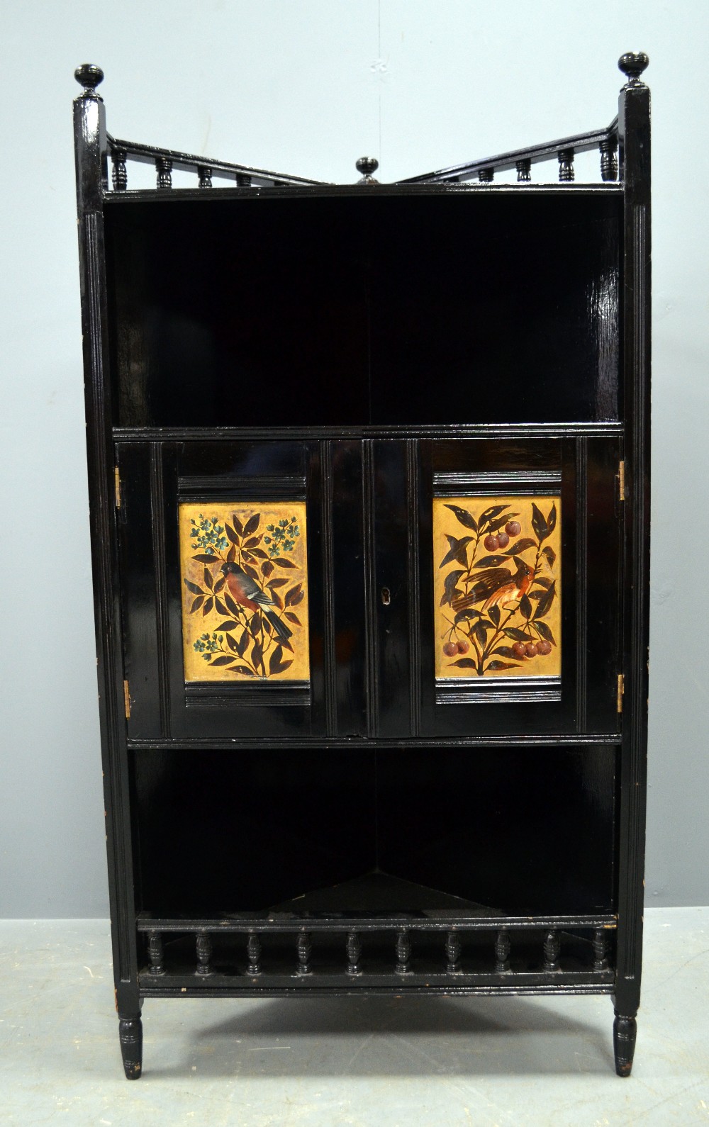 Ebonised corner cupboard in the manner of E. W. Godwin with gilt decorated panels depicting birds