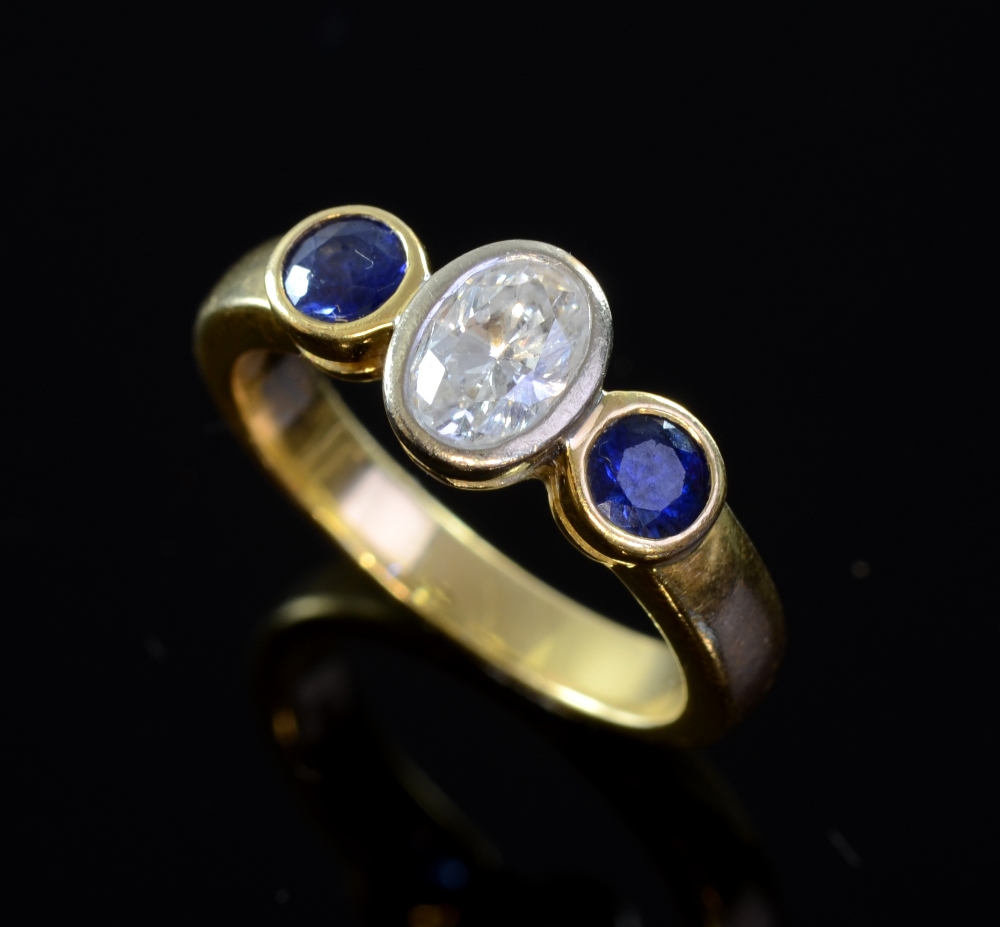 Sapphire and diamond set gold ring the central oval cut diamond .55 carat and two round sapphires in