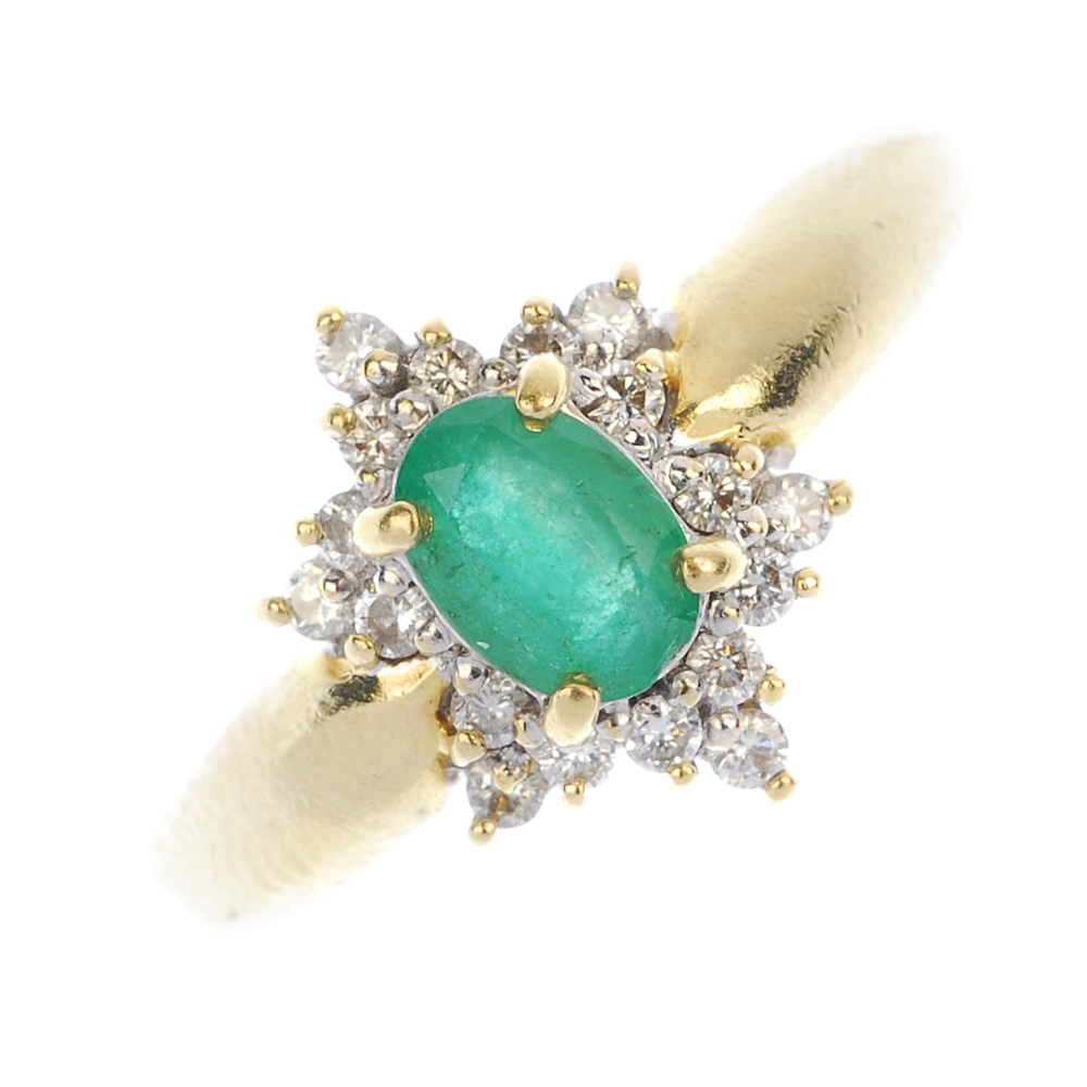 An 18ct gold emerald and diamond cluster ring. The oval-shape emerald, within a brilliant-cut