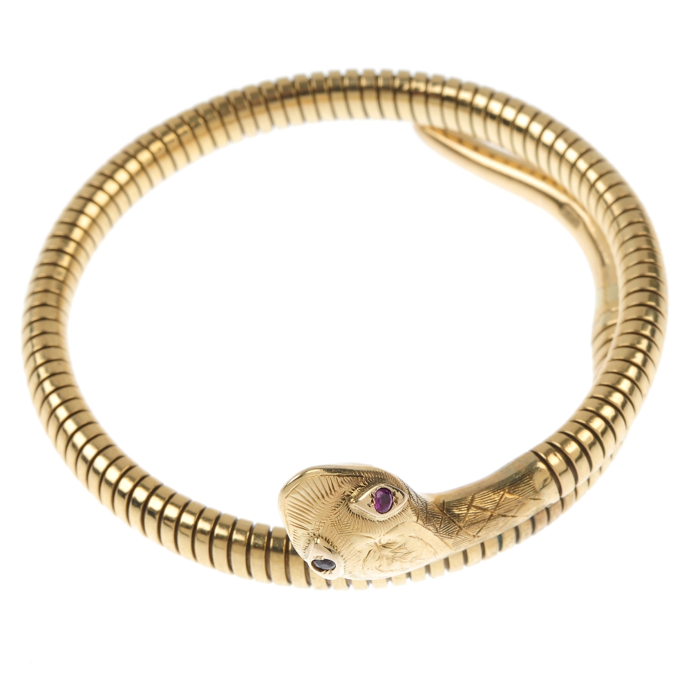 A mid 20th century 9ct gold ruby snake bangle. The engraved head with ruby eyes, to the coiled