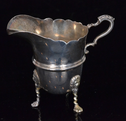 A hallmarked silver cream jug raised on three lion mask feet, terminating in a waved border and