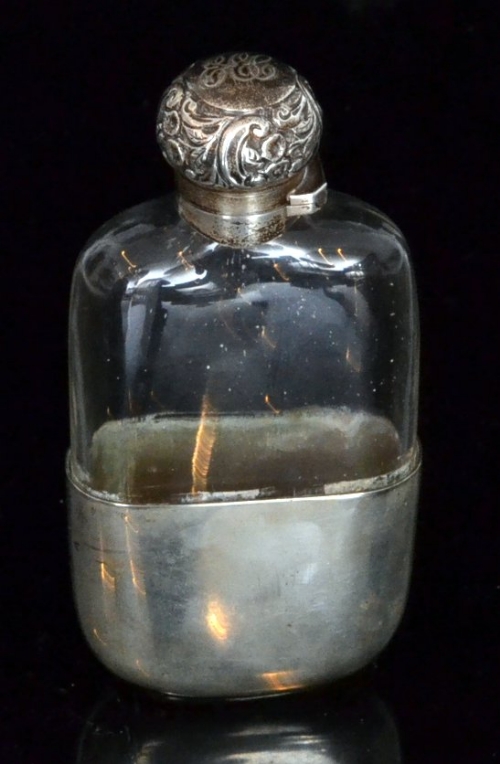 A late 19th Century hallmarked silver and clear glass hip flask, the hinged silver foliate embossed