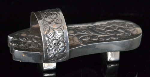 An early 20th Century white metal miniature study of a slipper with foliate engraved decoration to