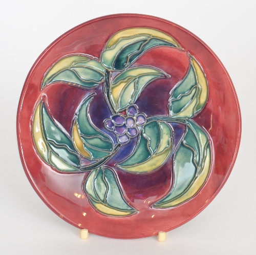Moorcroft Pottery - A shallow dish decorated with berries and foliage against a crimson ground,