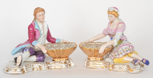 A pair of 20th Century table salts in the style of Meissen modelled as a lady and gentleman dressed