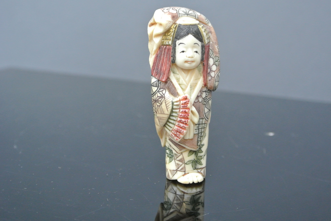 Japan School 19th century. A lovely carved and polychrome ivory netsuke in the form of a woman,