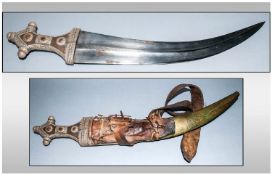 A Large Middle Eastern Shaped Dagger In An Engraved Brass Scabbard with silvered metal attachments