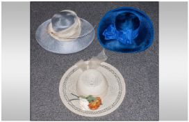 Three ladies wedding/occasion hats mostly blue in colour, presented in a hat box.