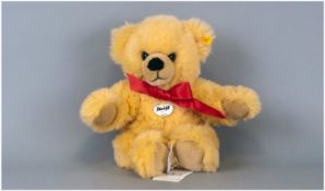 Steiff Bear `Bobby` yellow fur with red bow. Steiff button to ear with label & booklet still