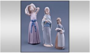 Lladro Figures ( 3 ) In Total. 1/ Girl Holding Her Hat, Height 10 Inches. 2/ Girl Holding Lilies