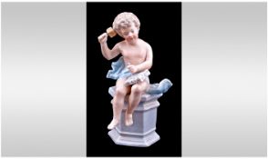 A Small Dresden Type Figure Of A Putti, sitting on a pedestal chiselling at a piece of marble.