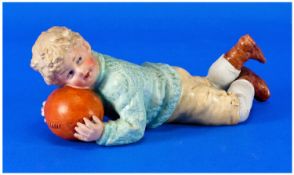 Heubach Figure - Young Boy Holding a Rugby Ball. Length 6 Inches.