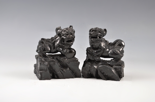 A pair of Chinese carved black stone models of ferocious kylins modelled respectively with a