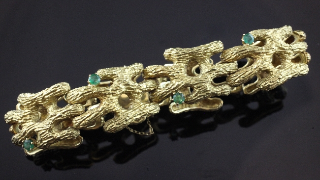 A textured 18ct gold and emerald articulated bracelet, with bark effect links and set with eight