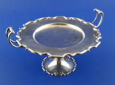 A George V silver two handled tazza, with curved handles, shaped border and shallow recess (ex.