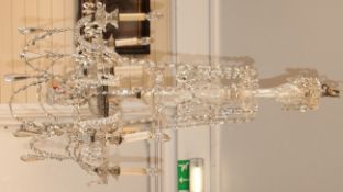 A large cut glass chandelier with six twisted scroll branches and leaf shaped sconces, with