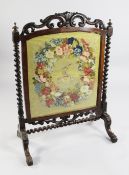 A Victorian rosewood fire screen, with floral needlework panel with central coat of arms, with