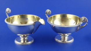 A George V silver sugar bowl and matching cream jug, of circular pedestal form, with flying scroll