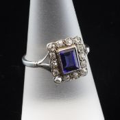 A 1920`s white gold, synthetic sapphire and diamond cluster ring, the emerald cut stone bordered