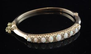 A gold, white opal and diamond hinged bangle, set with nine graduated oval opals, bordered with