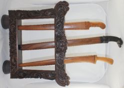 An Indonesian carved wood dagger or sword stand, containing three Indonesian or Malaysian swords,