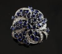 A white gold, sapphire and diamond cluster brooch, of pierced scroll form, set with round cut