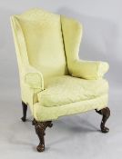 A Queen Anne style beech wing back armchair, upholstered in a yellow pattern fabric, with shell