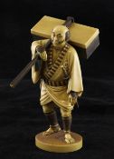 A Japanese tinted ivory figure of a samurai, early 20th century, standing and holding a case upon