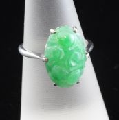 An 18ct white gold and jade dress ring, the oval stone carved with flowers, size L.