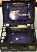 A George V fitted travelling case containing eighteen silver mounted items, including toilet jars