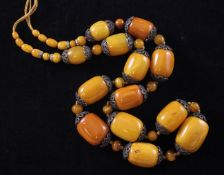 A single strand graduated barrel shaped amber bead necklace, with filligree base metal mounts,