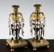 A pair of bronze and ormolu glass lustre candlesticks, with prismatic drops, on a square marble