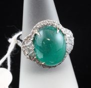 A white gold, cabochon emerald and diamond set cluster ring, the emerald weighing approximately 10.
