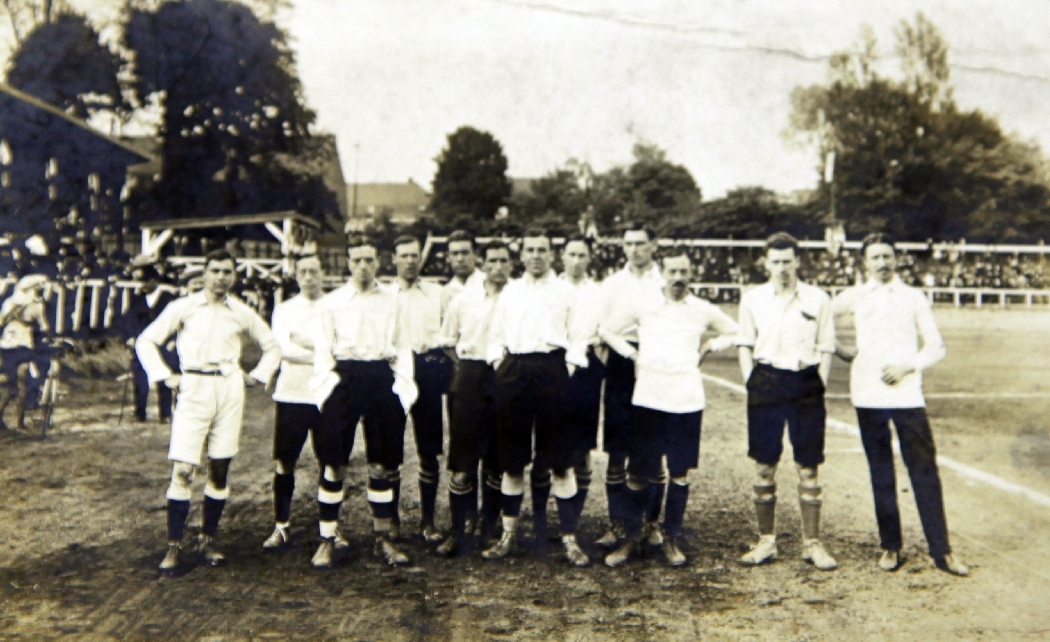 An English International football team postcard, depicting the players beside a football pitch,