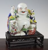 A Chinese famille rose model of Budai, seated with attendant boys, 21cm., wood stand