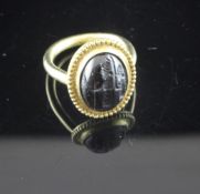 A Roman style gold and amethyst? ring, of oval form, carved with two figures with a staff, size P.