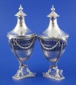 A pair of ornate George III pierced silver urn shaped mustard pots and domed covers, with engraved