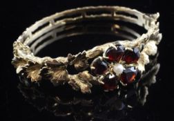A 9ct gold, garnet and seed pearl set hinged bangle, decorated with leaves and central motif set