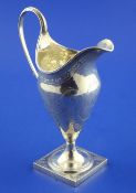 A George III silver helmet shaped cream jug, with engraved monogram and foliate decoration, on