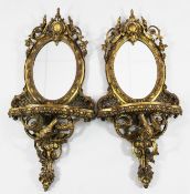 A pair of Victorian gilt wall brackets, with oval mirror backs and single serpentine shelf, with