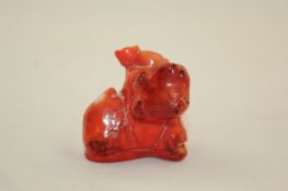 A Chinese red stained coral figure of Budai, seated beside a giant peach, 5.2cm.