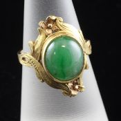 A gold and cabochon jadeite ring, with carve scroll setting, size L.