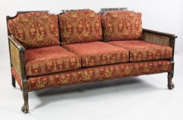 An Edwardian stained beech three seat bergere settee, with bell husk and floral rosette decoration,