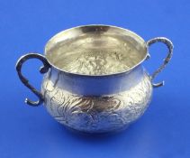 A Charles II silver porringer, with scroll handles and engraved initials and embossed with foliage,