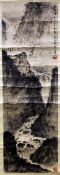 A Chinese scroll painting of a mountainous river landscape, with sages above a waterfall, inscribed